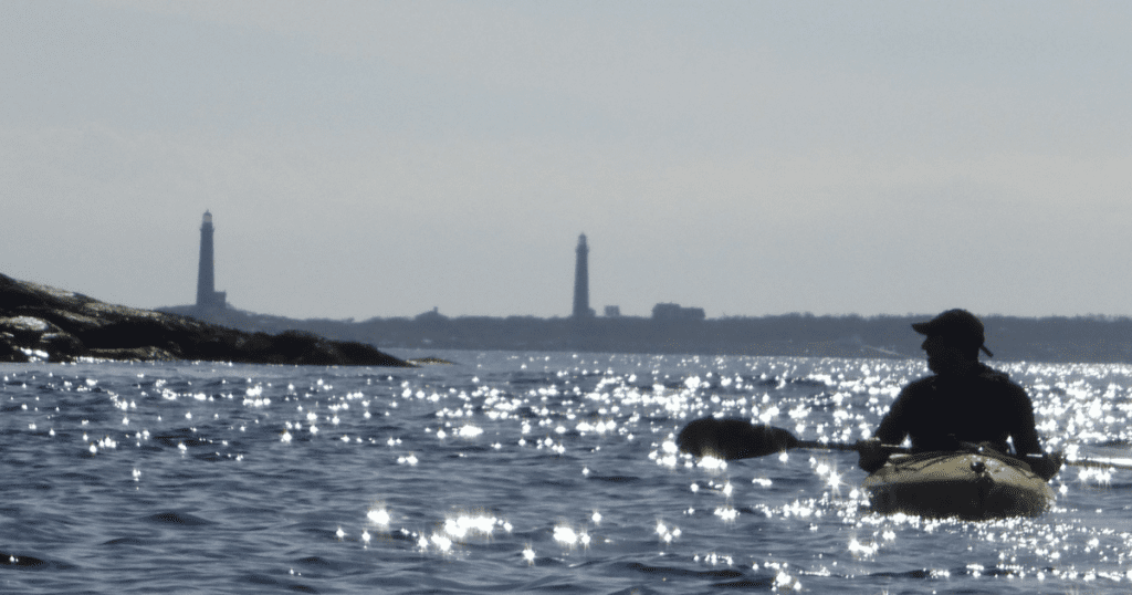 Adult kayaking with Thacher Island Twin Lighthouses in the background; off the coast of Rockport, MA.