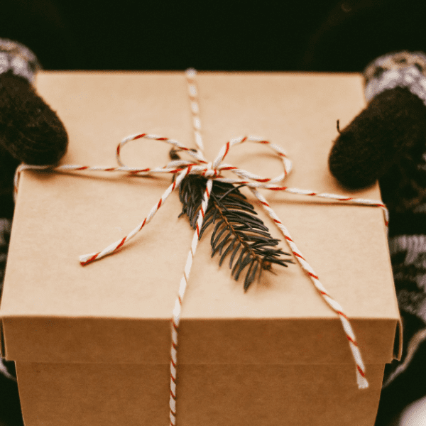 Holiday gifts wrapped in brown paper with red and white string, decorated with pinecones, red ornaments, and green pine needles