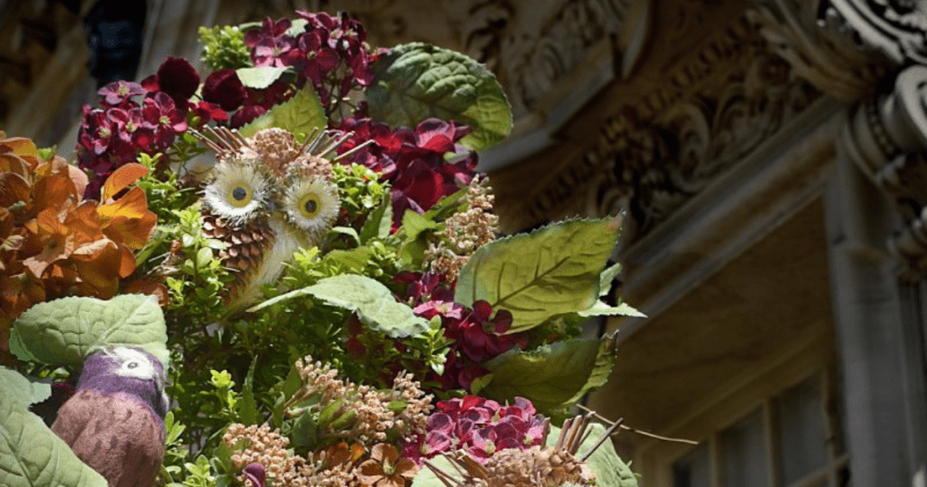 close up of an owl ornament within a larger bouquet of maroon flowers
