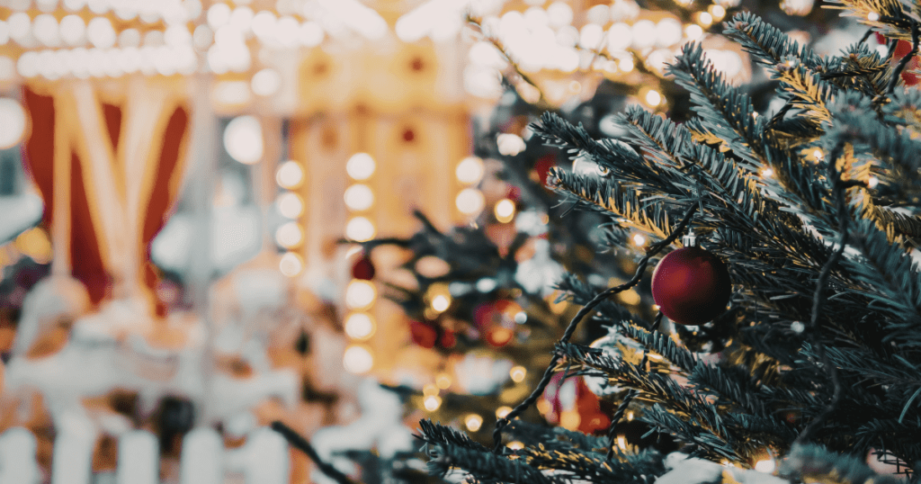 Close up of a Christmas tree with a carousel in the background at an outdoor holiday market in Massachusetts]