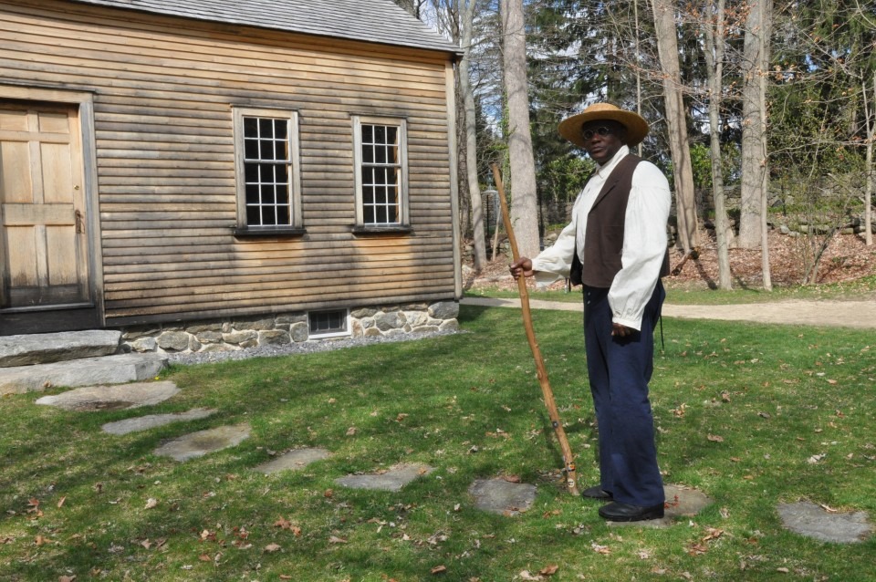 African American man standing in traditional clothing in front of the Robbins House
