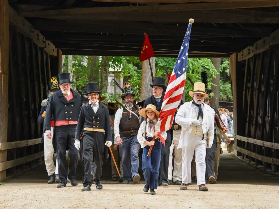 Old Sturbridge village reenactment walking across a bridge with the American Flag