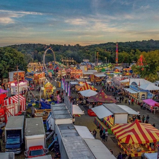 Aerial view of the Topsfield Fair at sunset with carnival rides and fairgrounds illuminated below.
