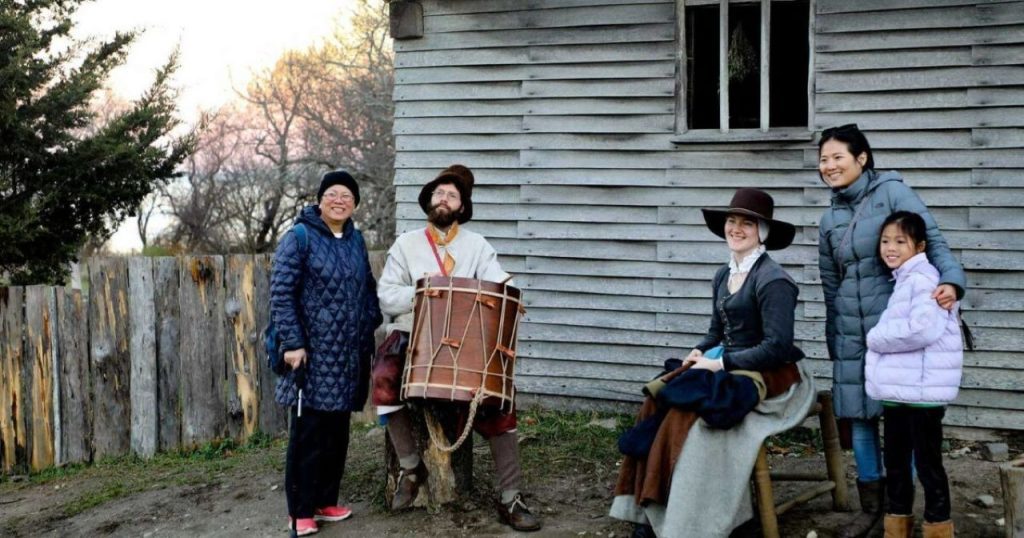A family visiting Plimoth Patuxet Museums and taking a picture with reenactors.